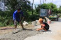 Anh Nguyễn Văn Khâm cùng con trai cần mẫn vá những “ổ voi”, “ổ gà” trên đường. Ảnh: Nhựt An - TTXVN