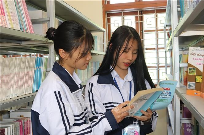 Nguyễn Tú Linh (bên phải) và bạn cùng lớp tìm hiểu kiến thức tại thư viện nhà trường. Ảnh: Quang Quyết-TTXVN