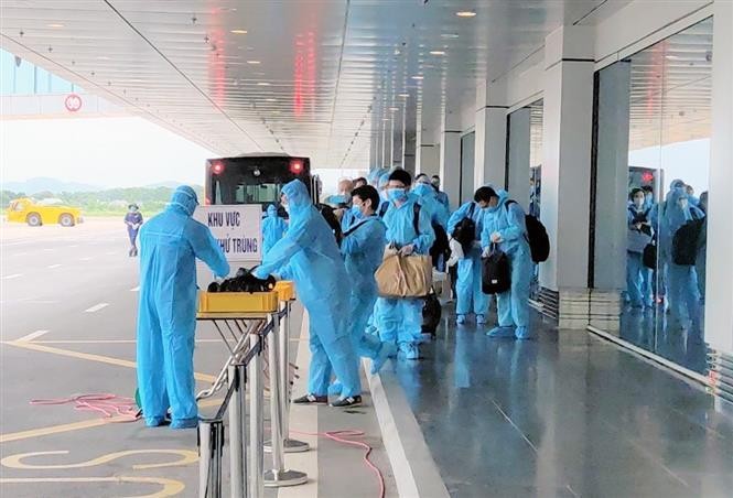 Các hành khách từ nước ngoài về đều mặc đồ bảo hộ y tế, tuân thủ các biện pháp phòng dịch, khi xuống máy bay và tiến hành khai báo y tế bắt buộc. Ảnh: TTXVN phát