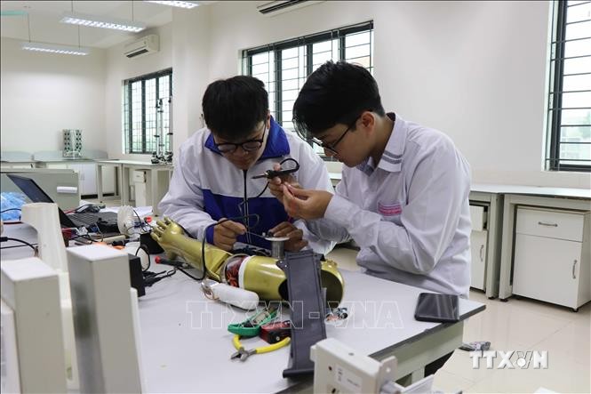 Phạm Đức Linh và Nguyễn Văn An cùng nhau nghiên cứu sản phẩm Cánh tay robot cho người khuyết tật liệt cơ tay toàn phần. Ảnh: Thanh Thương- TTXVN