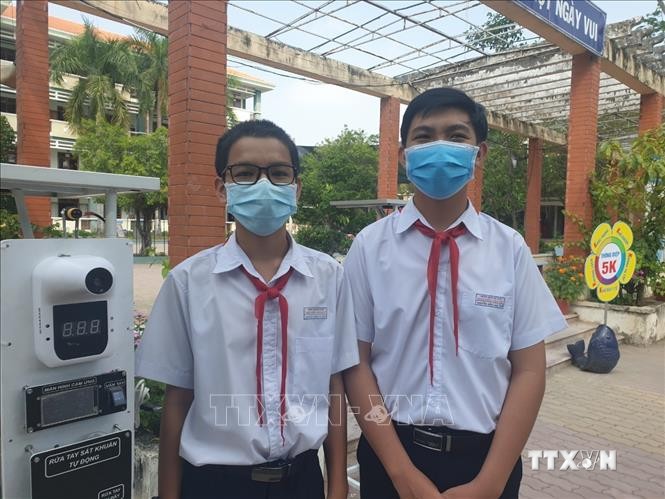 Em Nguyễn Thành Tài và em Nguyễn Điền Nam, Trường THCS Nguyễn Văn Cừ bên cạnh thiết bị đọc thân nhiệt và khử khuẩn tự động kết hợp điểm danh thông minh. Ảnh: TTXVN phát
