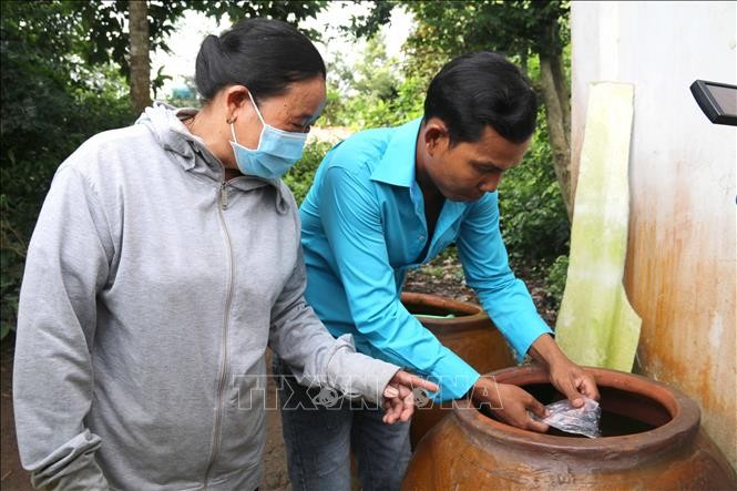 Các tuyên truyền viên hướng dẫn người dân xã Đa Lộc (Trà Vinh) thả cá lia thia vào lu chứa nước để diệt lăng quăng. Ảnh: Thanh Hòa - TTXVN